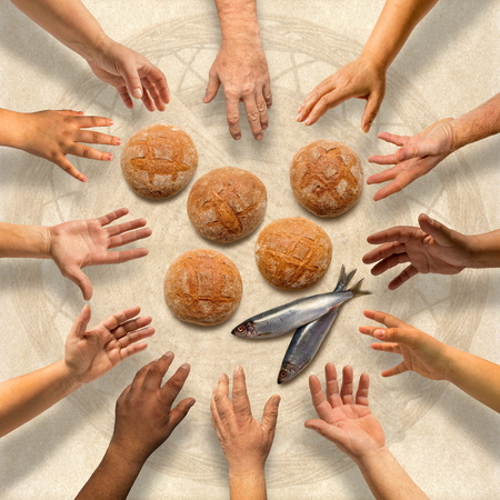 Hands stretching around five small barley loaves and two small fishの写真素材