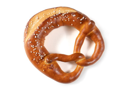 A Bavarian pretzel with salt on a white background. The pretzel is shaped like a knot and covered in a generous amount of salt. The pretzel is golden brown in color and looks crunchy and delicious.の写真素材