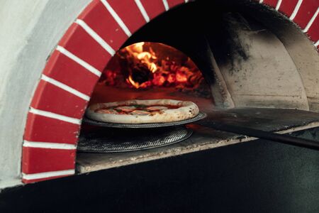 Cooked pizza is taken out on a shovel from an open wood burning stoveの写真素材
