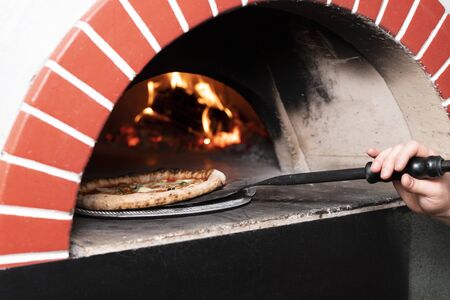 Cooked pizza is taken out on a shovel from an open wood burning stoveの写真素材