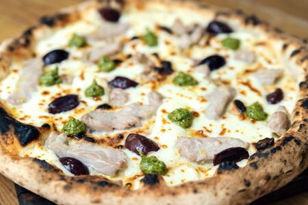 Freshly baked pizza with cheese, sauce, vegetables and meat on a wooden table close upの写真素材