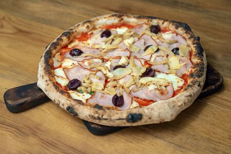 Freshly baked pizza with cheese, sauce, vegetables and meat on a wooden tableの写真素材