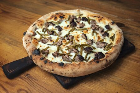 Freshly baked pizza with cheese, sauce, vegetables and meat on a wooden tableの写真素材