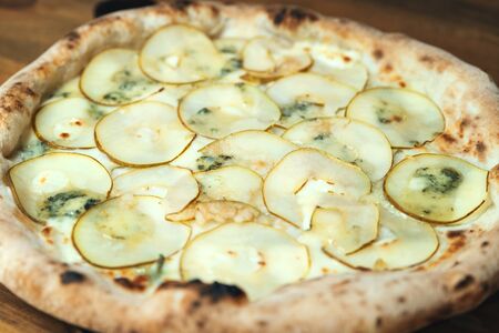 Freshly baked pizza with cheese, sauce, and pear on a wooden table close upの写真素材