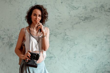 Curly-haired girl with a camera in her hands against the background of a textured wall.の写真素材