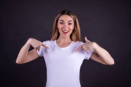 A shocked girl with an open mouth points her fingers at her t-shirt.の写真素材