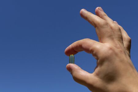 A man's hand holds a yellow capsule against a blue skyの写真素材