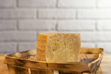 A piece of aged cheese on a wooden table against a brick wall.の写真素材