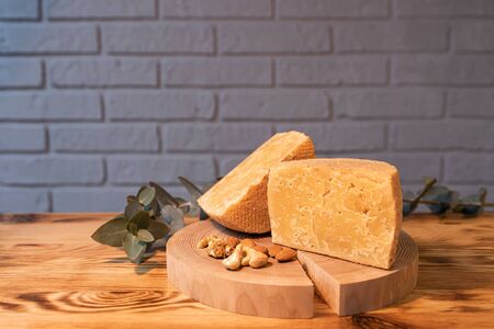 A head of aged cheese cut in half on a wooden Board with various nuts on the background of a brick wall.の写真素材
