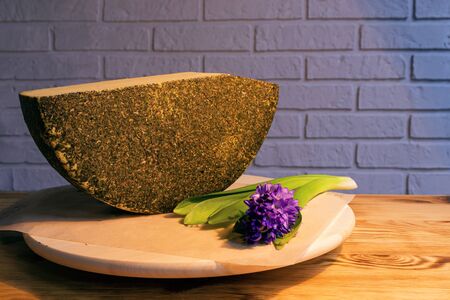A large piece of aged cheese with spices, next to a purple flower.の写真素材