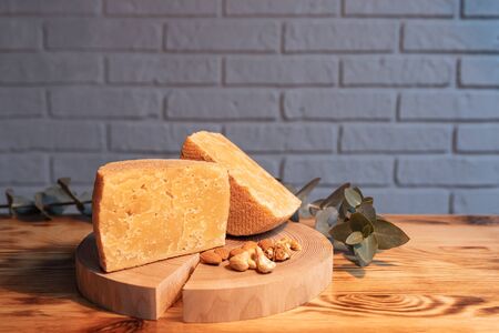 A head of aged cheese cut in half on a wooden Board with various nuts on the background of a brick wallの写真素材
