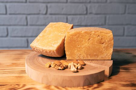 A head of aged cheese cut in half on a wooden Board with various nuts on the background of a brick wallの写真素材