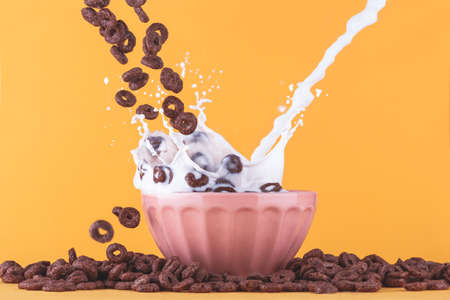 Milk cup on yellow background, with chocolate cereals falling around and milk splashing.の写真素材