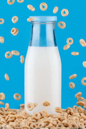 Milk bottle on blue background. Cereal rings falling around.の写真素材