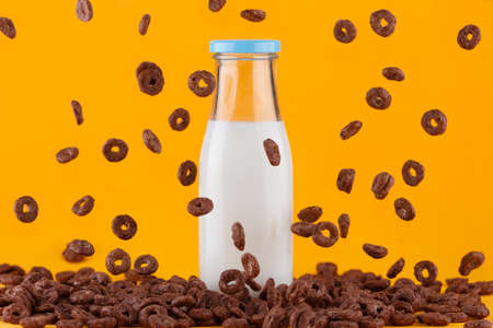 Milk bottle on yellow background. Chocolate cereals rings falling around.の写真素材