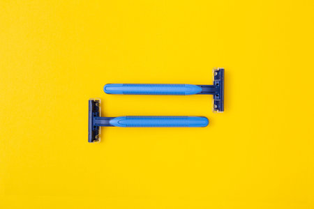 2 blue disposable razor blades, one opposite the other on a yellow backgroundの写真素材