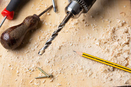 drill perched on a wooden board with shavings and other tools aroundの写真素材
