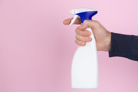 A man hand squeezing a spray bottle on a yellow background