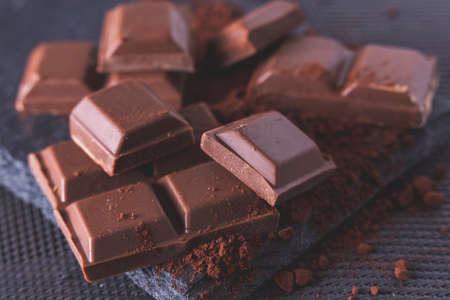 ounces of split chocolate on cocoa powder and black slate backgroundの写真素材
