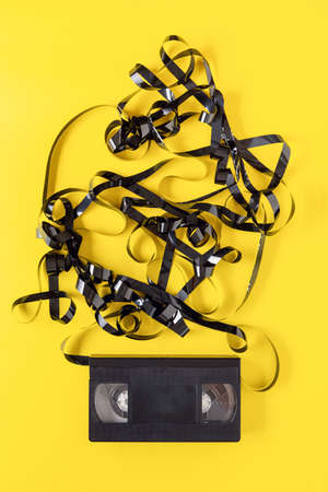 classic VHS videotape on a yellow background. The magnetic tape outside the case.の写真素材