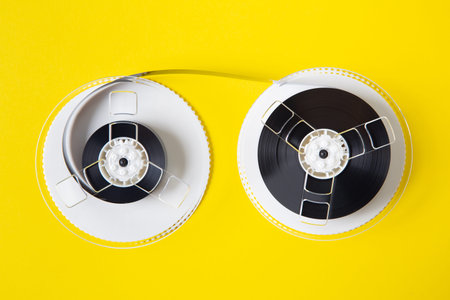 Reel of an old VHS videotape seen up close against a yellow background and meters of magnetic tape...