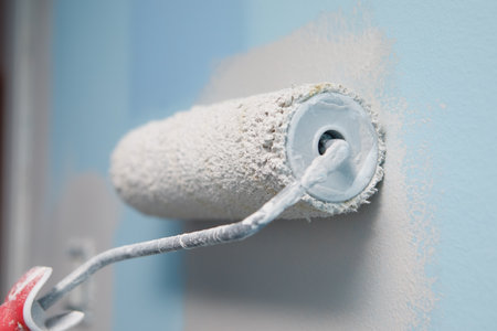 Close-up shot of a woman painting the wall of her house with a roller in a lighter color than the old oneの写真素材