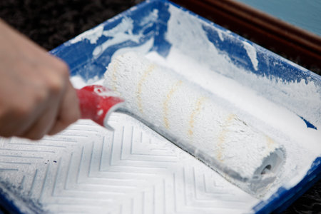 smearing paint roller in bucket with squeegee before painting wall