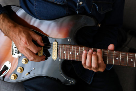 A man in the foreground practicing his electric guitar lessons at homeの写真素材