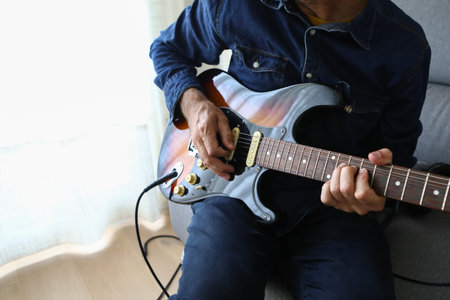 A man in the foreground practicing his electric guitar lessons at home