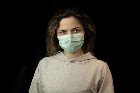 Studio portrait of young woman wearing a face mask, looking at camera, close up, isolated on black...