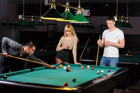 Young attractive people aim at game at billiardsの写真素材