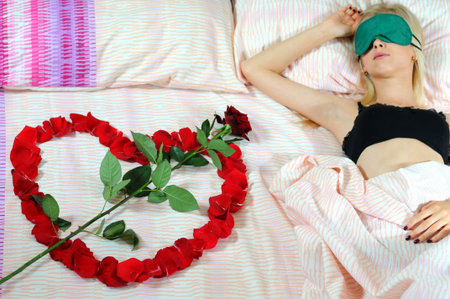 Woman lying in bed with a rose in the form of heartの写真素材