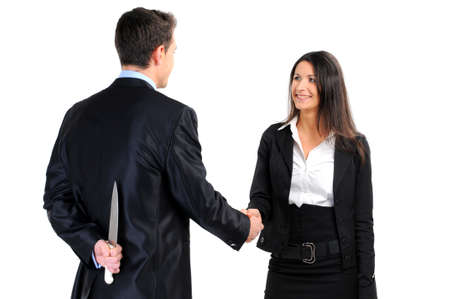 Portrait of business partners handshaking while male holding knife behind her backの写真素材