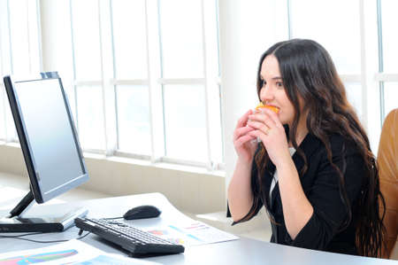 businesswoman eating a doughnut in her officeの写真素材