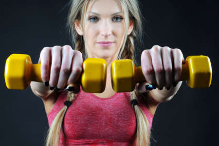 Torso of a young fit woman lifting dumbbells on dark backgroundの写真素材