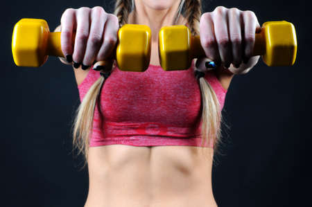 Torso of a young fit woman lifting dumbbells on dark backgroundの写真素材