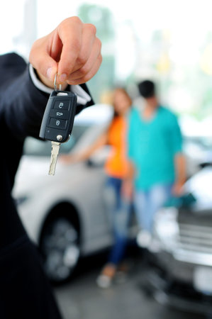 Handsome young classic car salesman standing at the dealership holding a key for a car