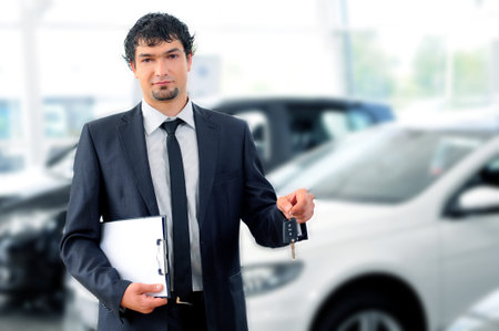 Handsome young classic car salesman standing at the dealership holding a key for a carの写真素材