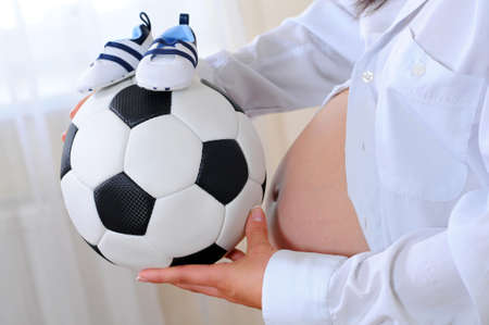 young pregnant woman with a soccer ball and athletic shoes for baby. waiting for the boyの写真素材