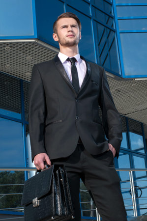 Portrait of a young businessman with briefcase in hand on background of office buildingの写真素材