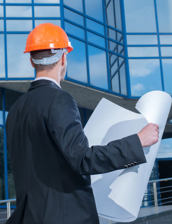 Young man working as engineer in new apartment buildings, looking at building plan in construction...