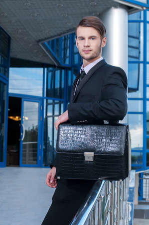 Portrait of a young businessman with briefcase in hand on background of office buildingの写真素材