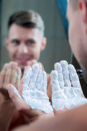 Reflection of a young man shaving in bathroom mirrorの写真素材