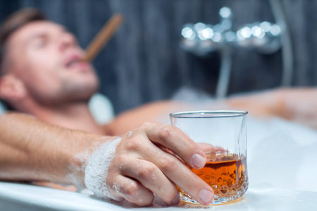 young man taking a bath, drinking whiskey and smoking cigar