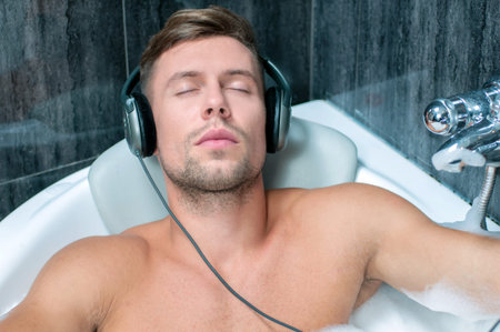 young man taking a bath, listening to music from the playerの写真素材