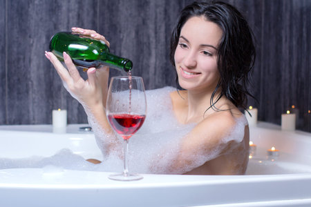A beautiful woman in a bath with foam drinking wineの写真素材