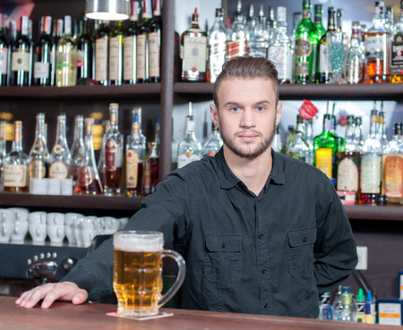 Young smiling bartender with beer on the barの写真素材