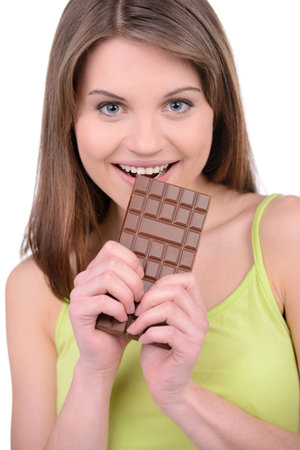 Portrait of a young woman eating a chocolate bar against a white background