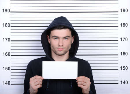 Busted burglar. Angry burglar holding a white poster while standing against police line-upの写真素材