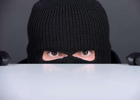 Evil criminal in a mask looking at the viewer. isolated on black backgroundの写真素材